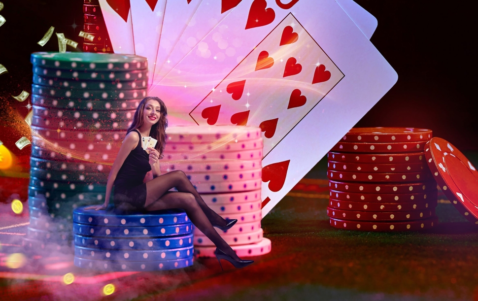 Brunette model in black dress is holding two aces, smiling, sitting on stacks of colorful chips on green playing table, against background with playing cards, flying dollars and coins. Poker, casino